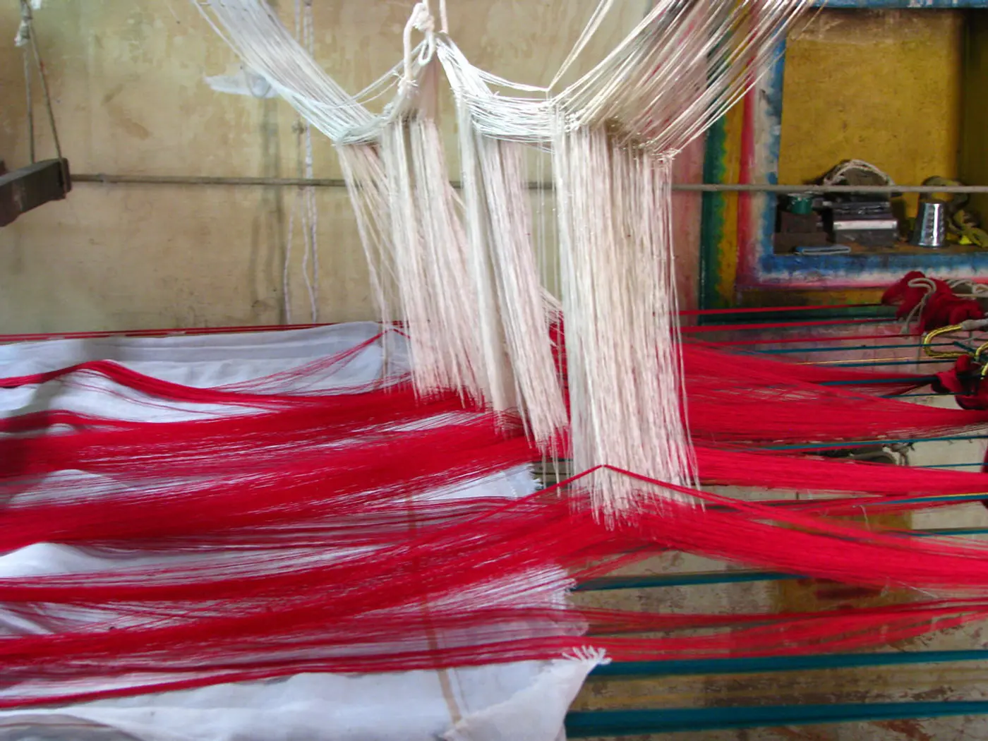 A narrow loom strung with red warp threads, the shuttle laid across the shed