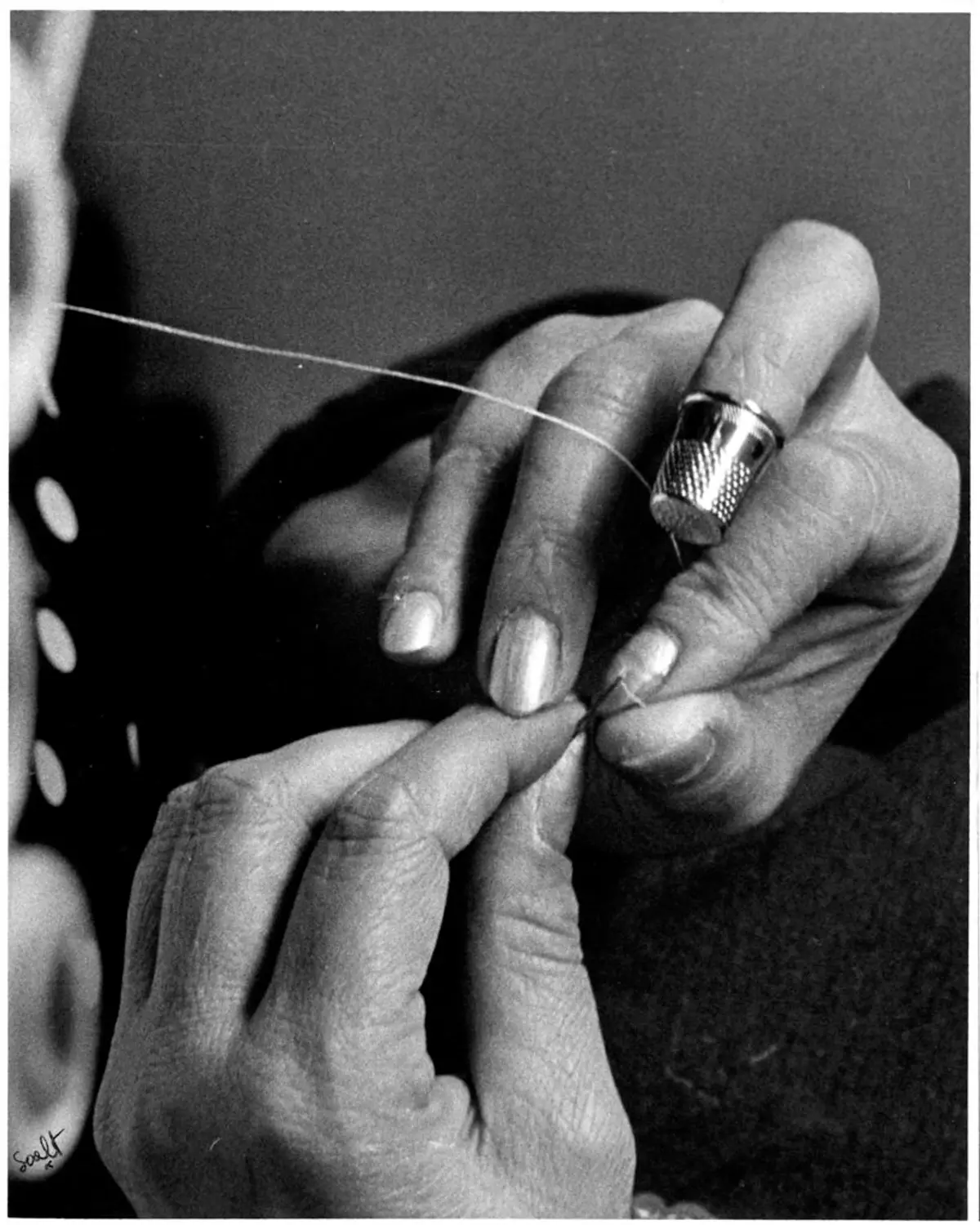 A maker's hands holding a half-finished panel, one finger keeping the count in the row