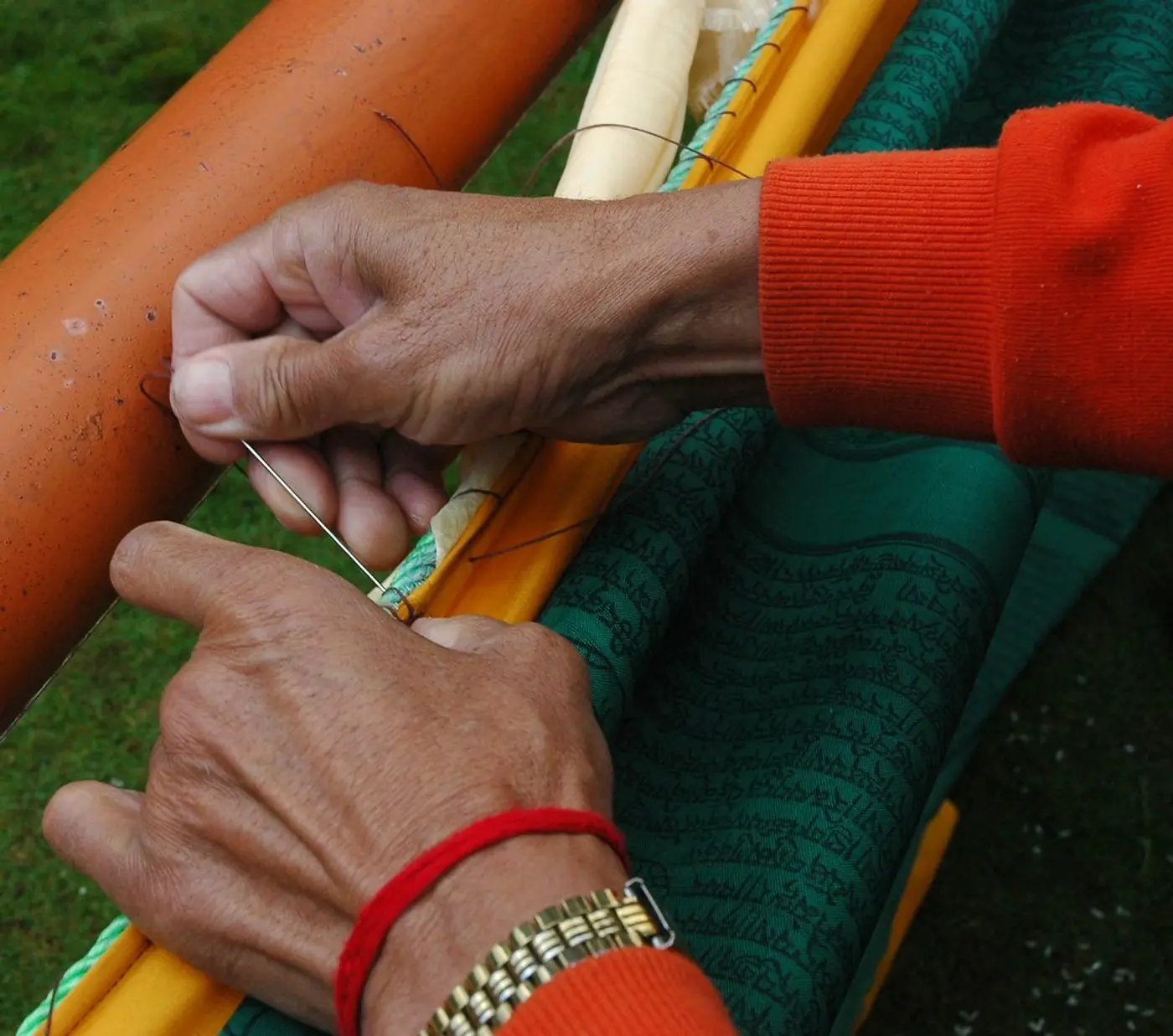 Two hands pulling a length of red thread taut across an embroidery frame