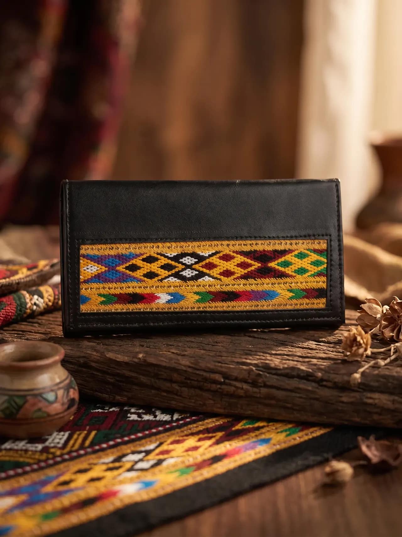 A black leather bifold wallet with a mustard yellow woven trim band in a diamond pattern